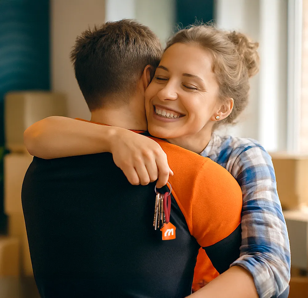 A joyful couple embracing in their new home, with the woman holding a set of keys featuring a house-shaped keychain, symbolizing the excitement of moving into a new place.